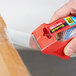 A hand using a red 3M Scotch heavy-duty tape dispenser to apply tape to a box.