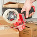 A hand using a red and black 3M Scotch tape dispenser to seal a box.