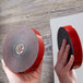 A hand holding a roll of 3M Scotch black mounting tape with red and black label.