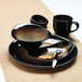 A black bowl from a Libbey Reserve Tiger Porcelain dinnerware set on a table with a place setting including a fork and spoon.
