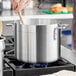 A silver Choice Standard Weight Aluminum Stock Pot on a stove with a wooden spoon in it.