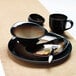 A Libbey Tiger Organic Porcelain saucer on a table with a black bowl and plate.