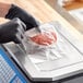 A person in black gloves weighing a piece of meat on a scale.