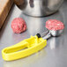 A yellow Vollrath #20 squeeze handle ice cream scoop filled with a meatball.