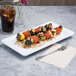 A white rectangular melamine platter with grilled chicken skewers and vegetables on a table.