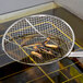 A Thunder Group round mesh skimmer removing fried fish from a frying pan.