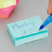 A hand using a blue pen to write on a 3M Cape Town Collection Post-It note.