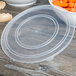 A clear plastic Fineline bowl lid on a table over a bowl of carrots.