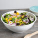 A white high profile plastic catering bowl filled with salad and vegetables.