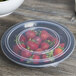 A Fineline black plastic catering bowl filled with strawberries on a wood surface.