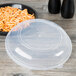 A clear plastic catering bowl lid on a table over a bowl of noodles.