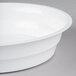 A Fineline white low profile plastic serving bowl on a gray surface.