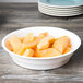A white Fineline low profile plastic serving bowl filled with sliced melon on a wood surface.
