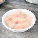 A white Fineline low profile plastic serving bowl filled with sliced melons on a wood table.
