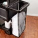 A black Rubbermaid cart with a mesh bag full of towels.
