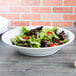 A white low profile plastic catering bowl filled with salad on a table.