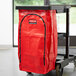 A red Rubbermaid janitor cart bag with a black zipper on a cart.
