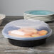 A black Fineline low profile plastic serving bowl filled with food on a table.