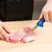A hand using a Mercer Culinary Millennia Colors® narrow boning knife to cut meat on a cutting board.