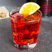 An Anchor Hocking Regency double old fashioned glass with red liquid, ice, and a slice of orange.