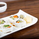 An American Metalcraft curved edge porcelain serving platter with sushi rolls on a table.