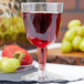 A Fineline clear plastic wine goblet filled with red liquid next to grapes and strawberries.