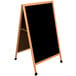 An Aarco oak A-frame sign board with a black write-on marker board and wooden frame.