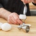 A hand using a Matfer Bourgeat stainless steel egg topper to scoop an egg.