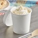 A white Choice paper food cup filled with ice cream with a wooden spoon on the side.