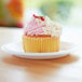 A cupcake with pink frosting and white swirls on a white Eco-Products compostable plate.