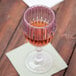 A customizable fluted wine glass filled with pink liquid on a table.