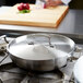 A stainless steel low domed lid on a Vollrath saute pan.