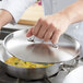 A person holding a Vollrath low domed metal lid over a pan of food.