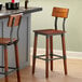 A Lancaster Table & Seating rustic bar height chair with a metal frame and wooden seat and legs next to a counter.