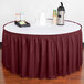 A table with a white table cloth and a burgundy shirred pleat table skirt with velcro clips on a table.