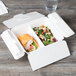 A white Eco-Products Folia compostable takeout container with a sandwich and salad inside.