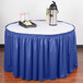 A Wyndham royal blue shirred pleat table skirt on a table with a blue tablecloth.