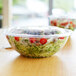 A clear plastic Eco-Products salad bowl filled with salad on a table.