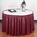 A round table with a burgundy shirred pleat table skirt and a tray of coffee and a thermos.