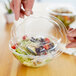 A person's hands placing a plastic lid on a clear plastic salad bowl.