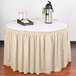 A bone Snap Drape shirred pleat table skirt on a table with a white tablecloth and a tray of food.