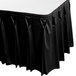 A black Snap Drape Wyndham table skirt with pleated edges on a table outdoors.