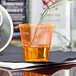A Fineline Quenchers neon orange hard plastic shot cup filled with orange liquid on a table.