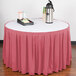 A table skirt with a dusty rose color on a table with a red tablecloth and a tray of food on it.