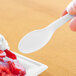 A hand holding a white Eco-Products Plantware compostable plastic spoon over a dessert.