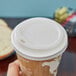 A hand using an Eco-Products white compostable plastic hot cup lid on a coffee cup.