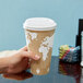 A hand using an Eco-Products white compostable plastic lid on a coffee cup.