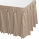 A beige Snap Drape Wyndham table skirt with pleated edges on a table with a white cloth.