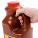 A hand holding a gallon of Louisiana Wildly Wicked Buffalo Wing Sauce with a red cap.