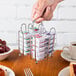 A hand holding a Tablecraft chrome plated rack of jelly packets on a hotel buffet table.